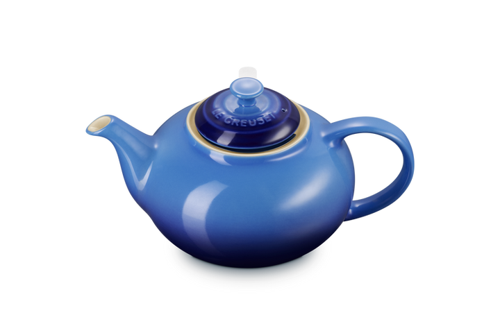 Blue Le Creuset teapot with a lid on a white background