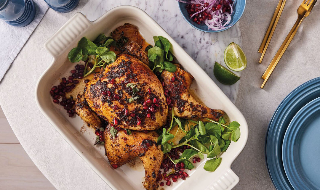 Roasted chicken with garnishes on a white platter with a blue plate and lime wedge in the background.