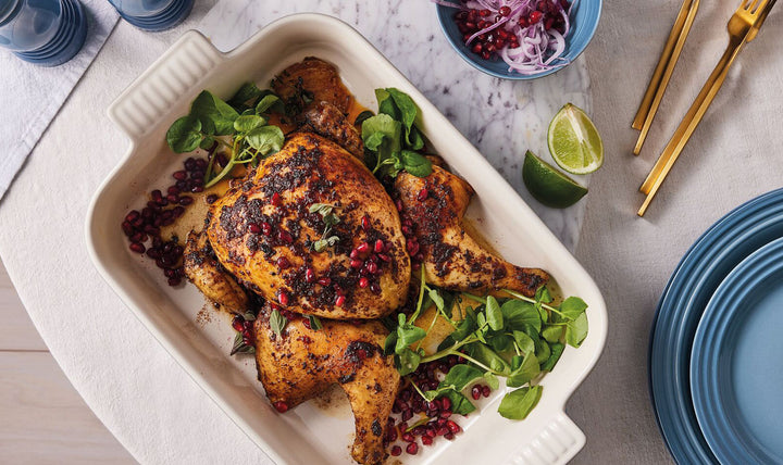 Roasted chicken with garnishes on a white platter with a blue plate and lime wedge in the background.