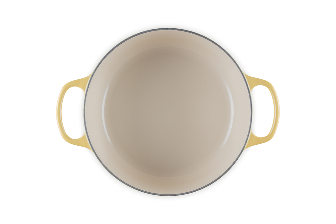 Beige enameled cast iron cookware with yellow handles on a white background