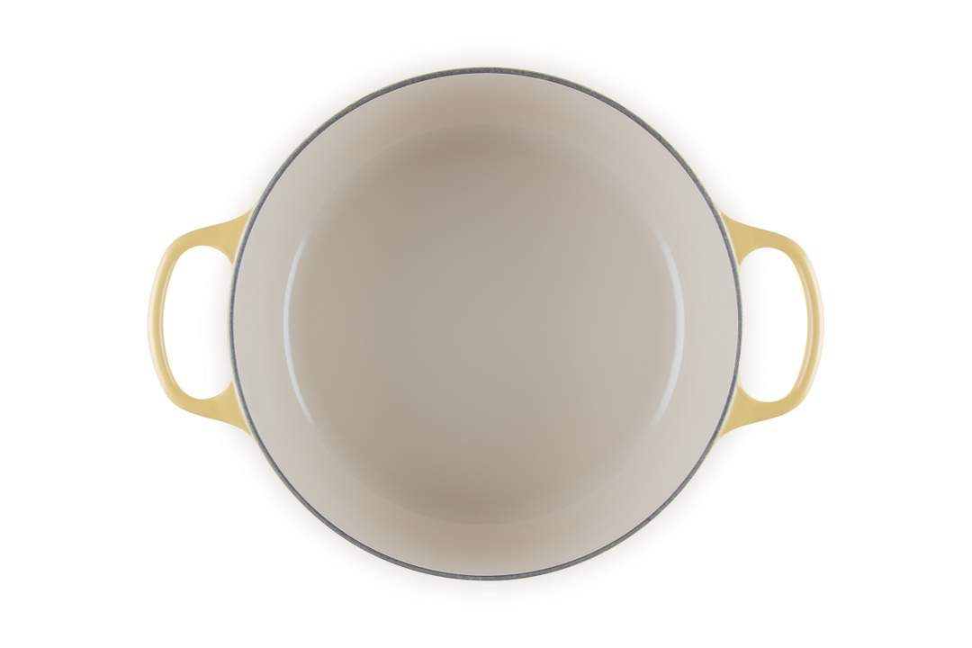 Beige enameled cast iron skillet with yellow handles on a white background