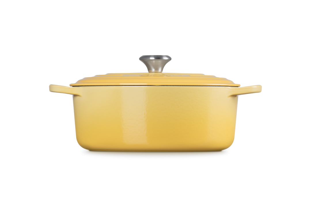 Yellow cast iron oval casserole with a lid on a white background