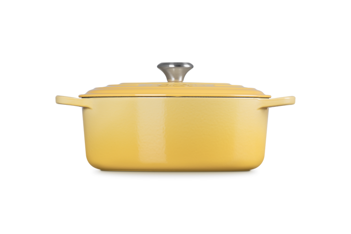 Yellow cast iron oval casserole with a lid on a white background