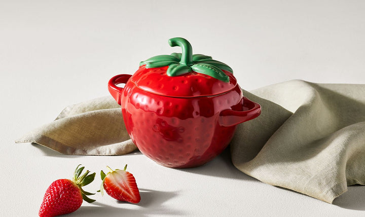 Red strawberry-shaped pot with green lid on a light background