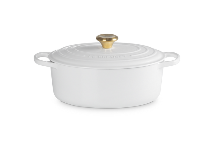 White oval ceramic cookware with gold lid knob on a white background
