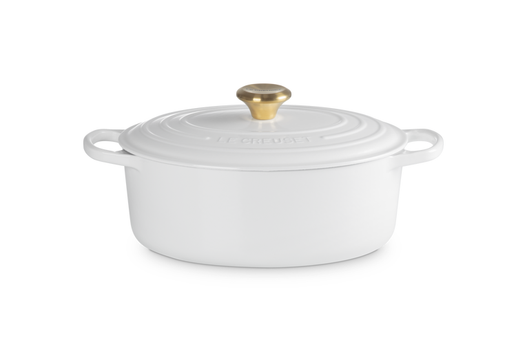 White oval ceramic cookware with gold lid knob on a white background