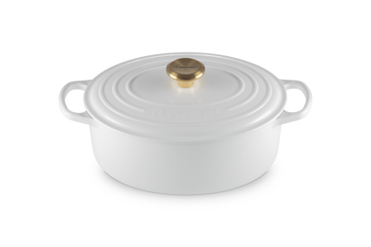 White oval ceramic cookware with gold lid on a white background