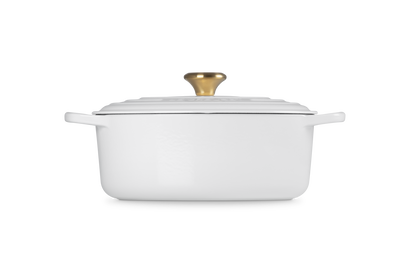 White oval ceramic cookware with gold lid knob on a white background