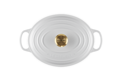 White oval ceramic cookware with gold lid knob on a white background