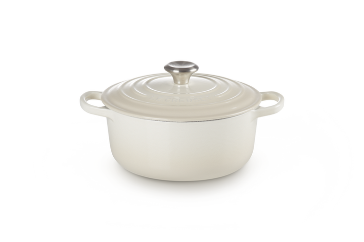 Cream enameled cast iron Dutch oven with a lid on a white background