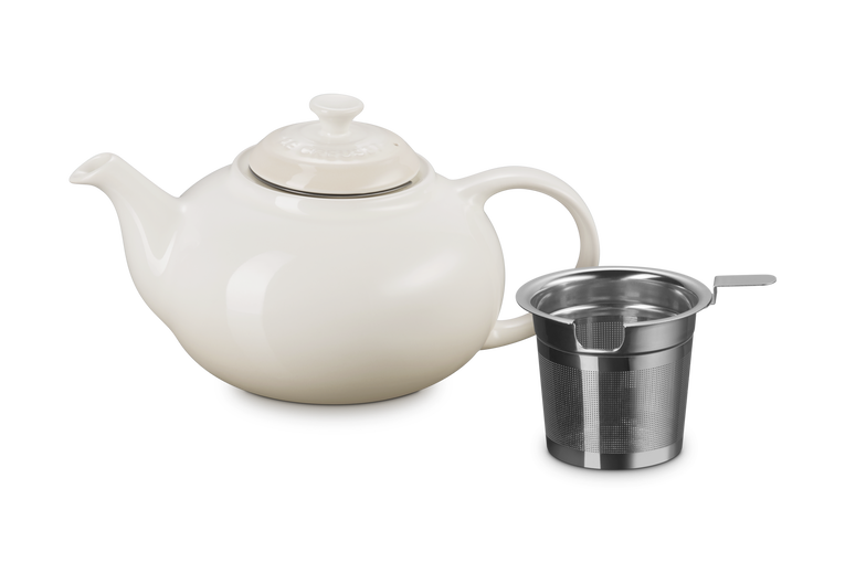 Le Creuset cream ceramic teapot with a metal infuser basket on a white background