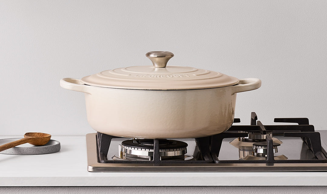 Beige ceramic cookware on a stove with a white background