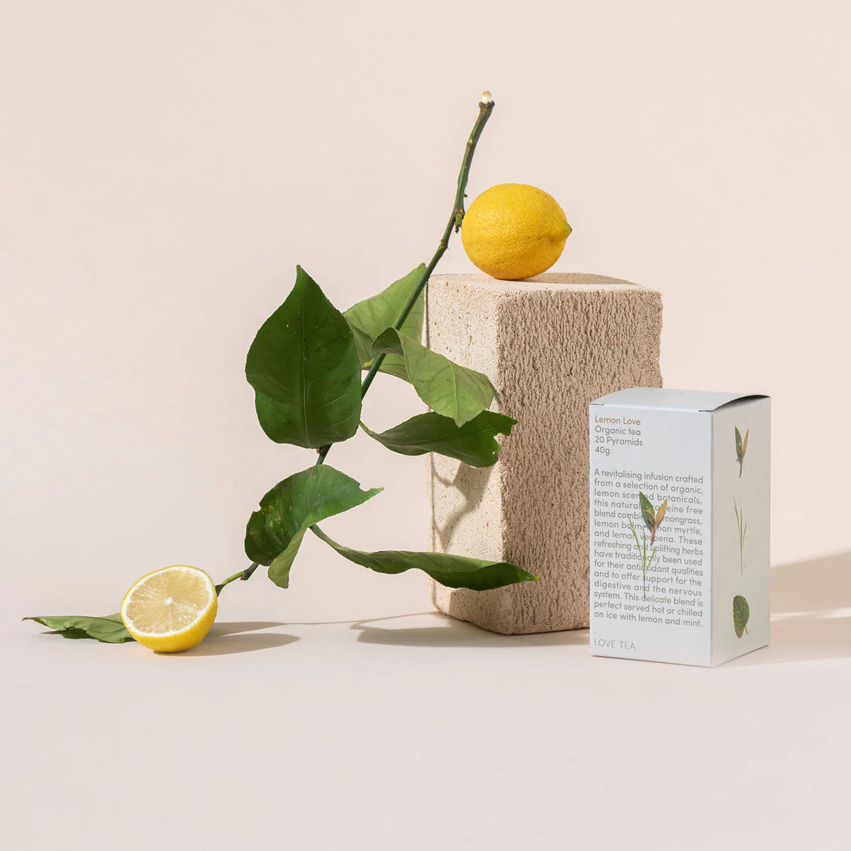 Two lemons and a box of Love Tea Lemon Love teabags on a textured surface with a light background