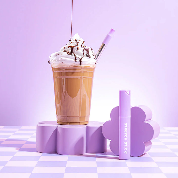 An iced coffee with cream and a stainless steel straw on a purple check surface &amp; purple background