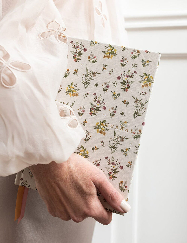 Hand holding a floral-patterned notebook with a pencil