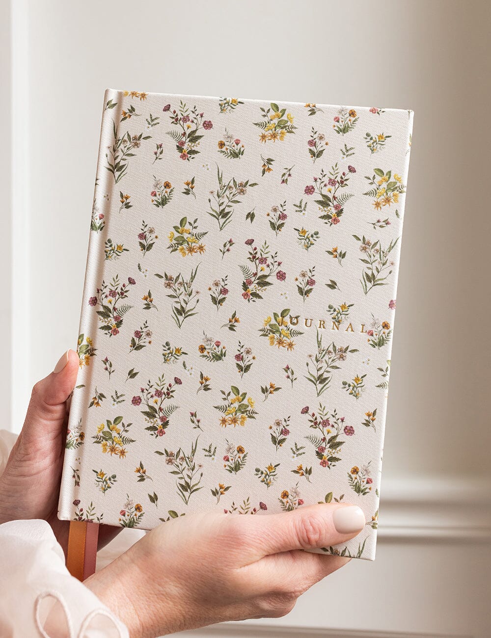 Hand holding a floral-patterned journal against a neutral background