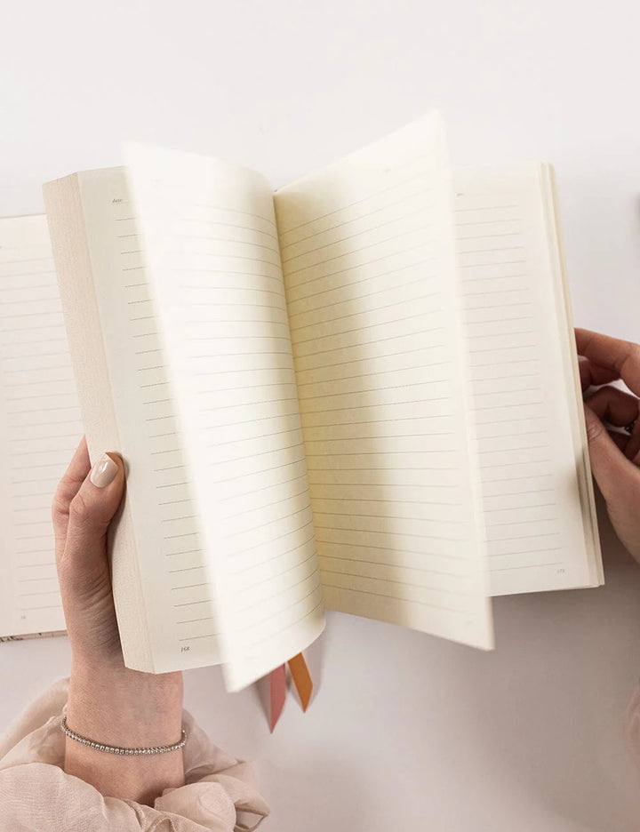 Person holding an open notebook with lined pages on a light background