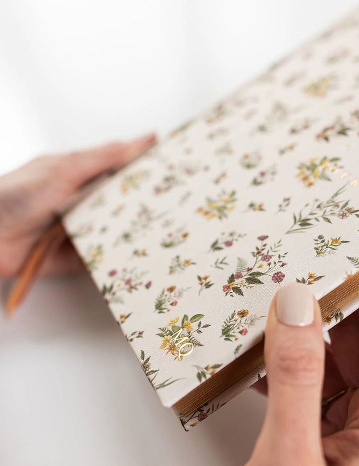 Hand holding a floral-patterned notebook on a white background