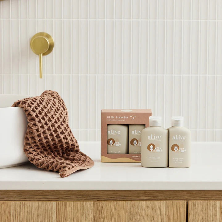 Bathroom setting with 'alive' body care products and a brown textured towel on a white surface.