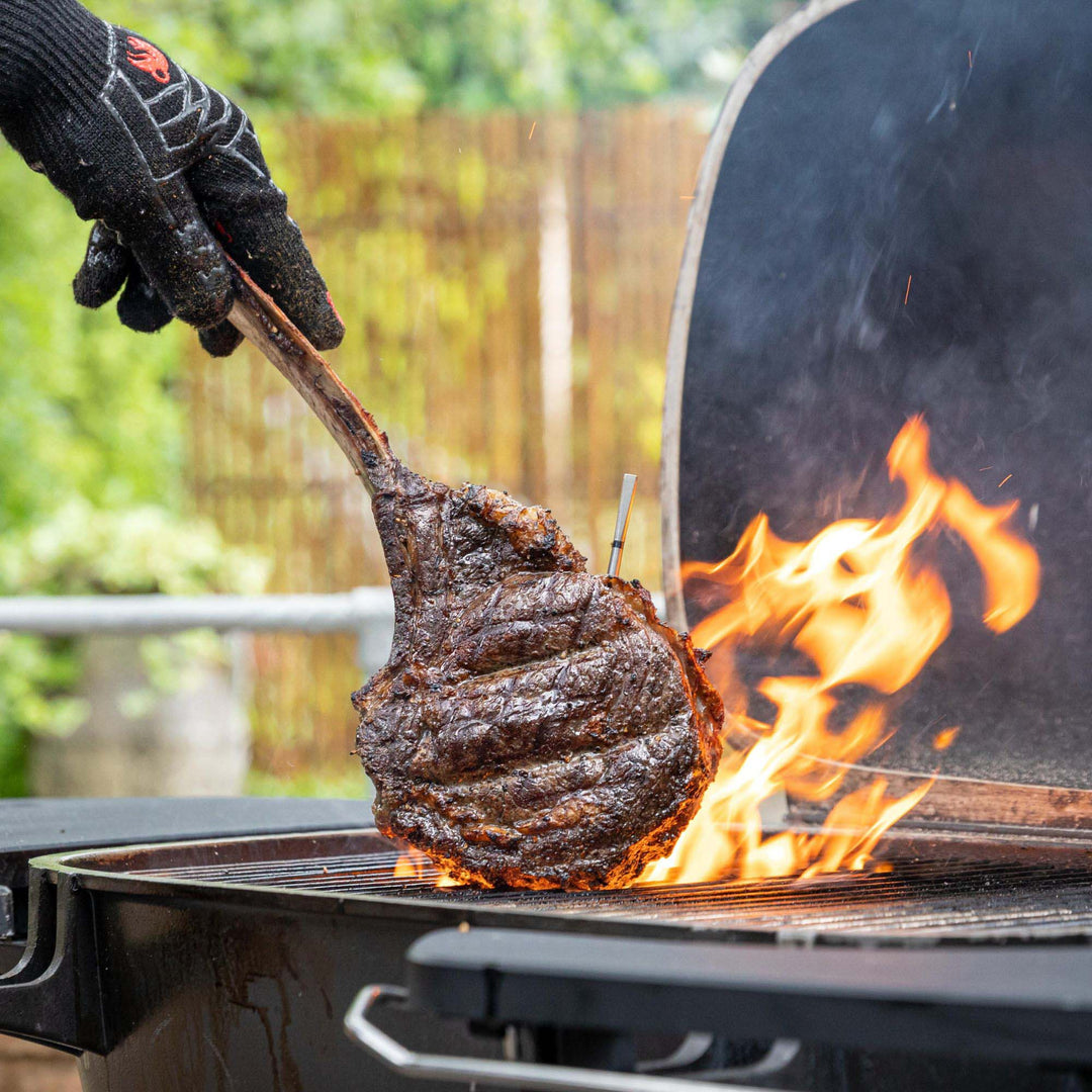 Person grilling a steak over an open flame on a barbecue