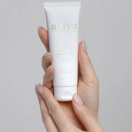 Hand holding a white tube of 'alive' cream against a gray background