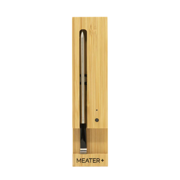 A wireless smart meat thermometer by MEATER, placed vertically in a wooden-looking case with a black probe.