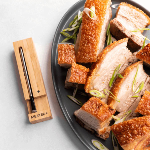 Meater Plus thermometer next to a plate of crispy pork belly on a grey plate