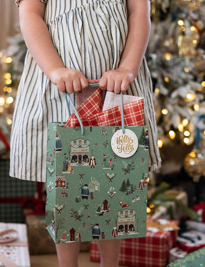 Child holding a festive gift bag with a Christmas tree and presents in the background