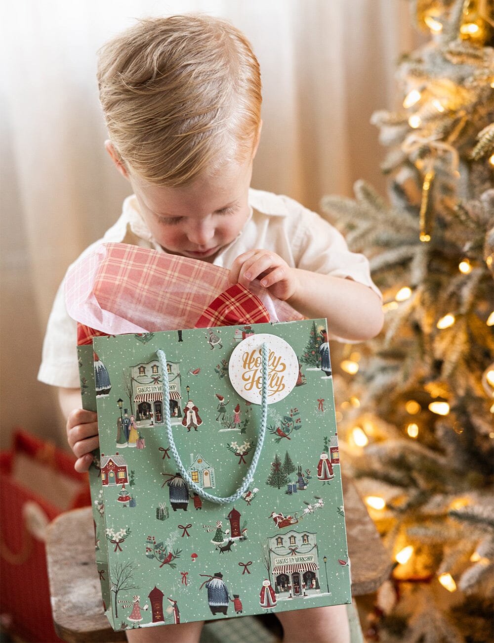 Child opening a gift bag with a Christmas tree in the background