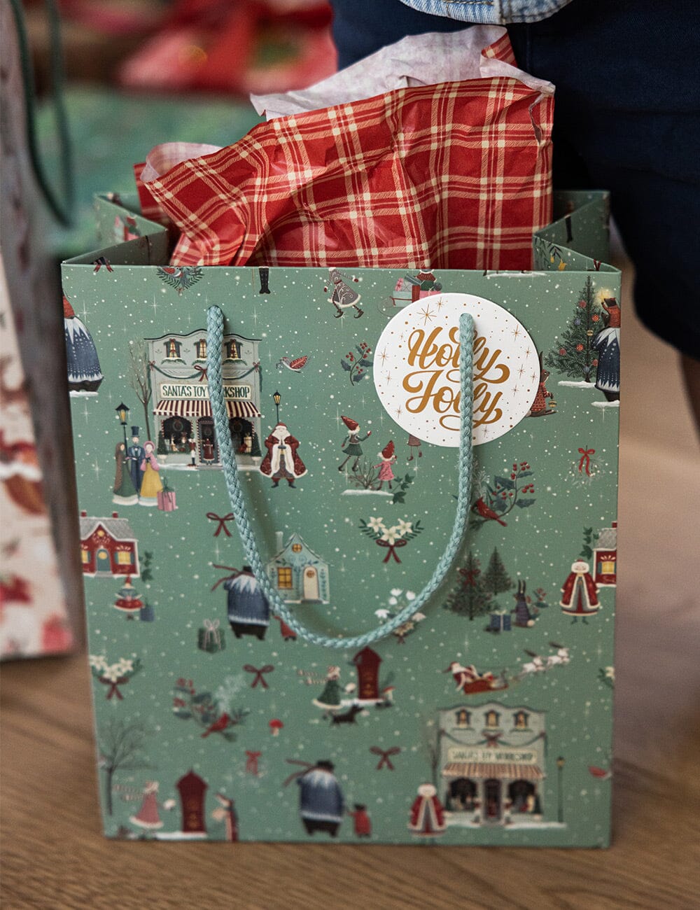 Green gift bag with festive design and 'Merry Holly' label on a wooden surface.