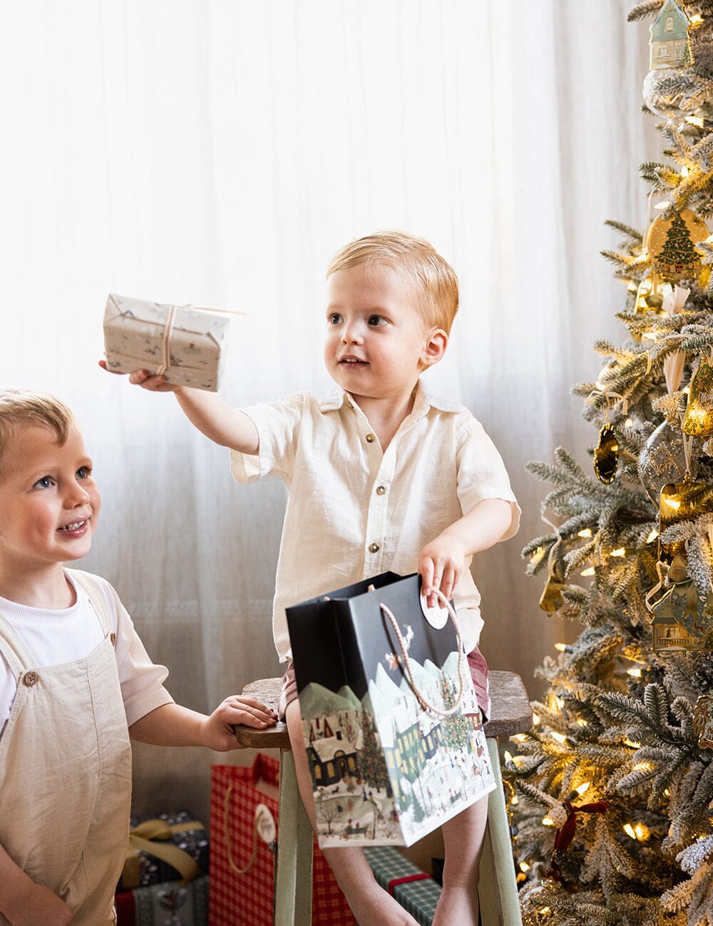 Two children by a decorated Christmas tree with presents.