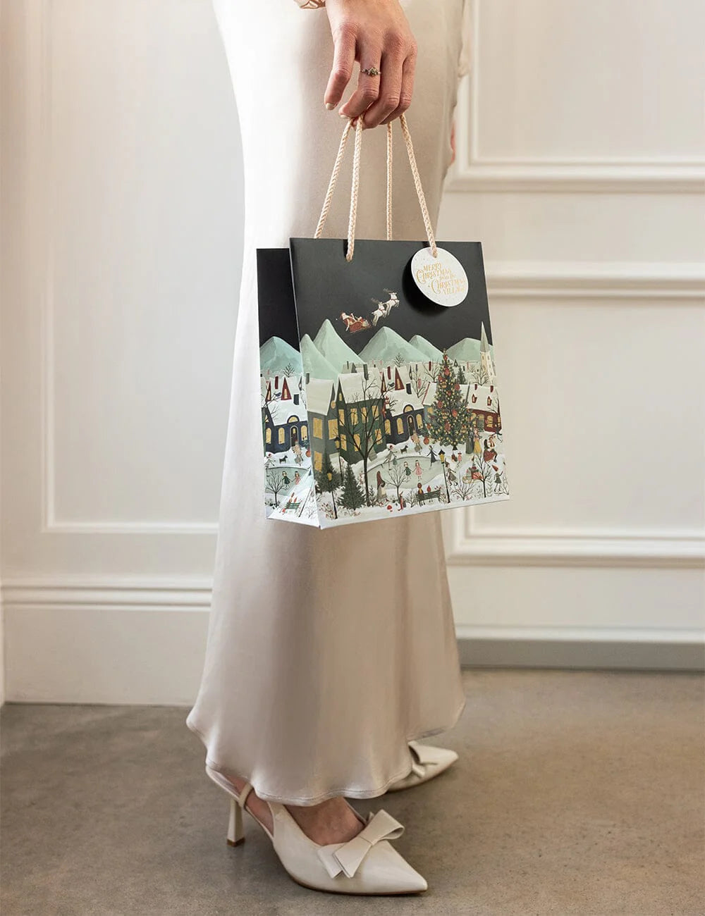 Person holding a decorative shopping bag with a scenic design against a white wall.
