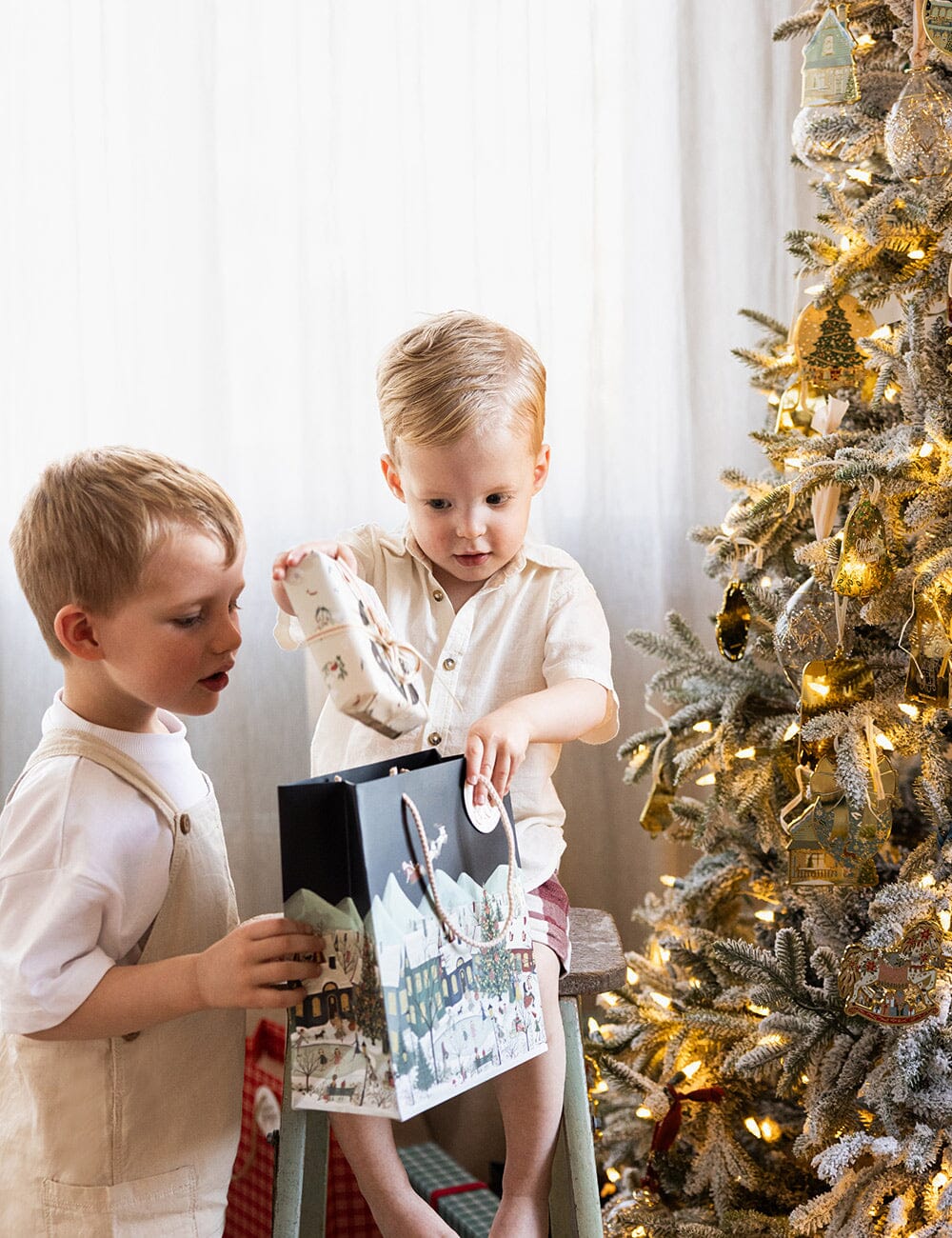 Two children opening a gift in front of a decorated Christmas tree.