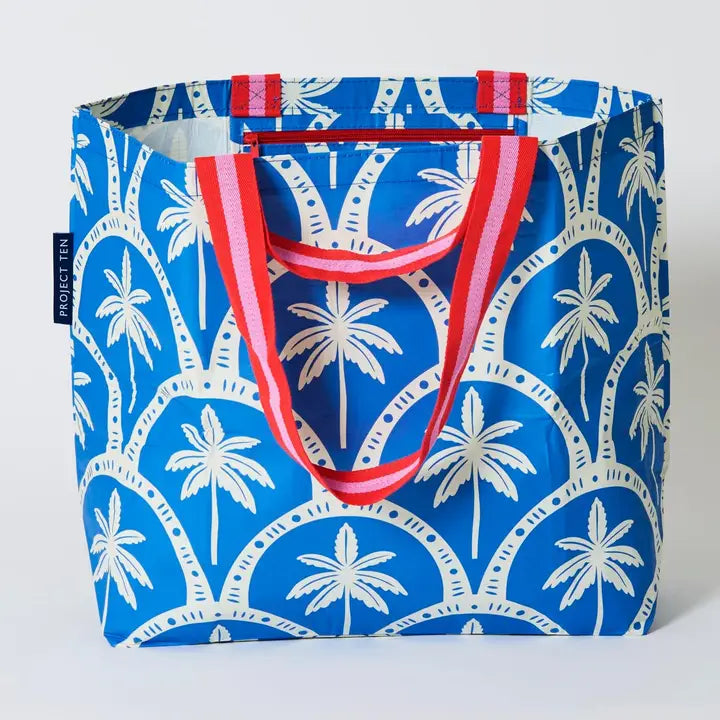 Blue tote bag with palm tree pattern and red handles on a white background
