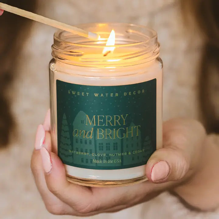 Candle with a 'Merry and Bright' label being lit by a wooden wick.