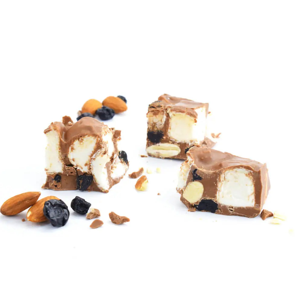 Chunks of milk chocolate rocky road with marshmallows, almonds and dried bluberries on a white background