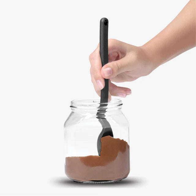 Hand holding a spoon over a jar of chocolate spread with a white background