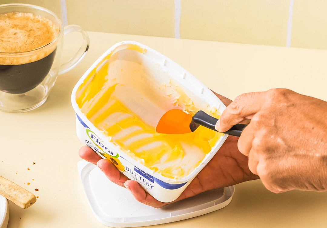 Person scooping butter with a spoon, next to a cup of coffee on a light-colored surface.