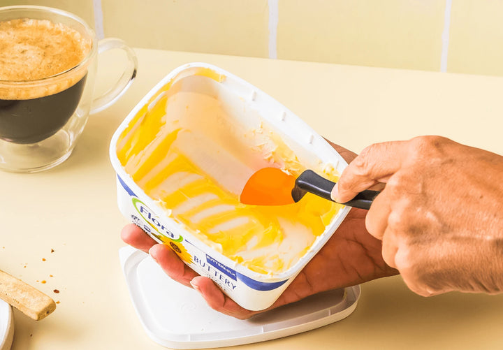 Person scooping butter with a spoon, next to a cup of coffee on a light-colored surface.