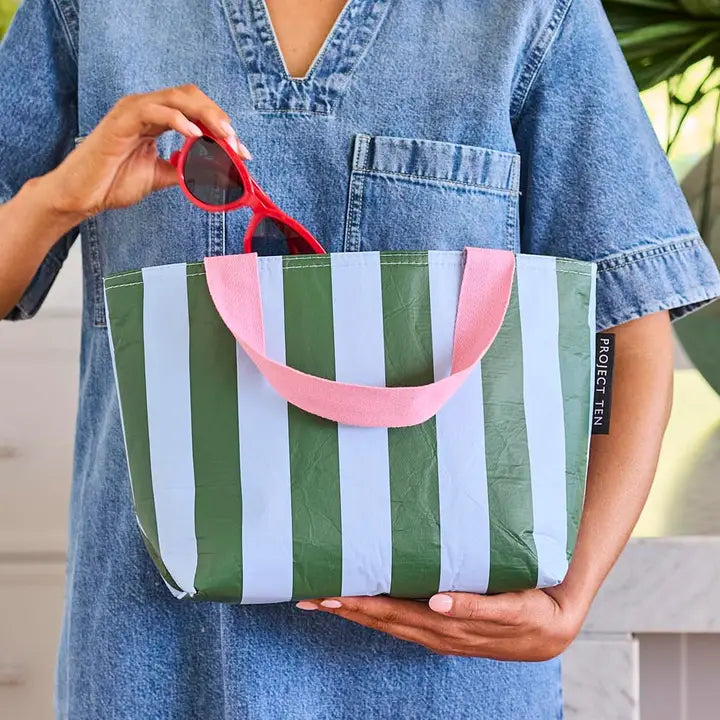 Person holding a green and pink striped bag with sunglasses, wearing a denim shirt.