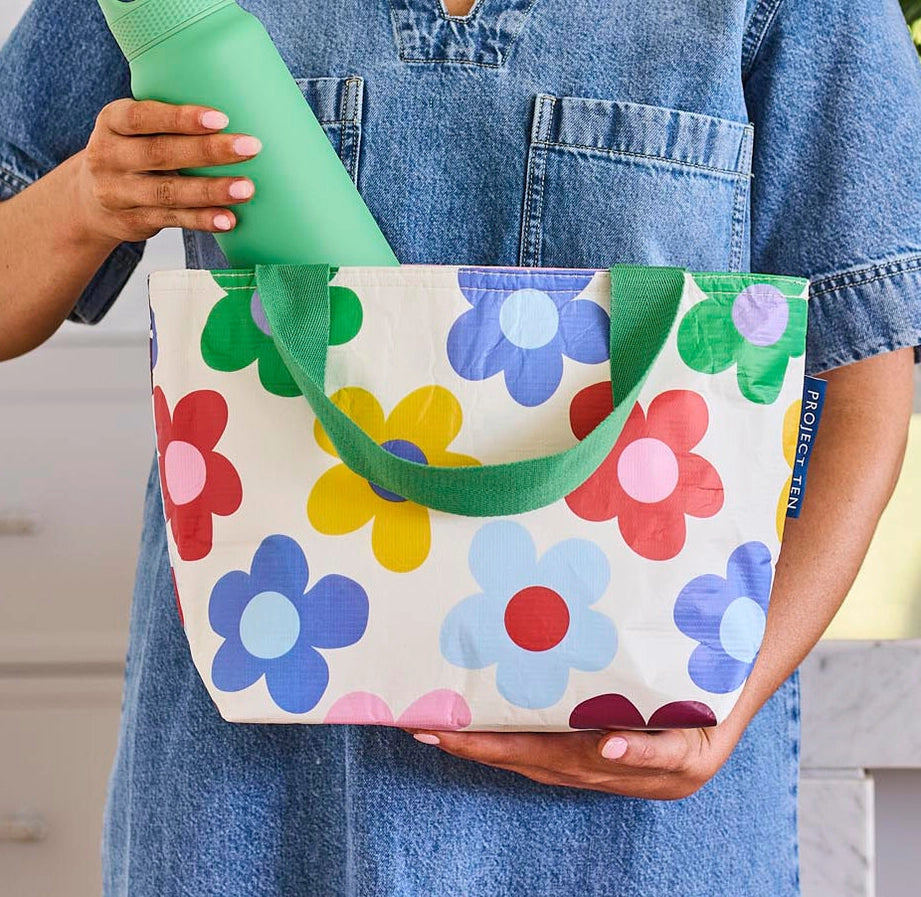 Person holding a colorful floral tote bag with a green handle.