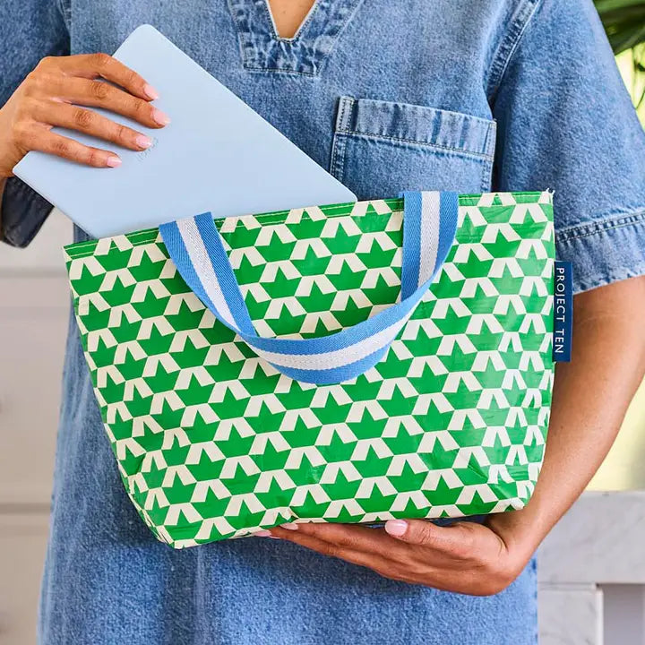Person holding a green geometric patterned bag with blue handles