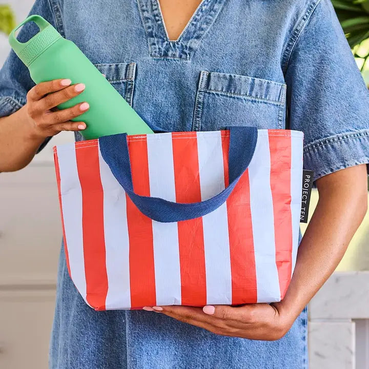 Person holding a red, white, and blue striped bag with a green bottle.