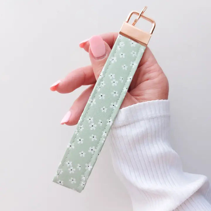 Hand holding a light green fabric strap with a rose gold buckle against a white background