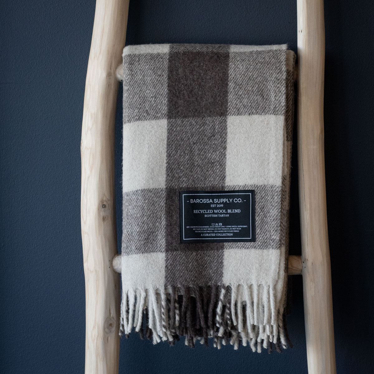 Plaid blanket with a label on a wooden ladder against a dark blue wall