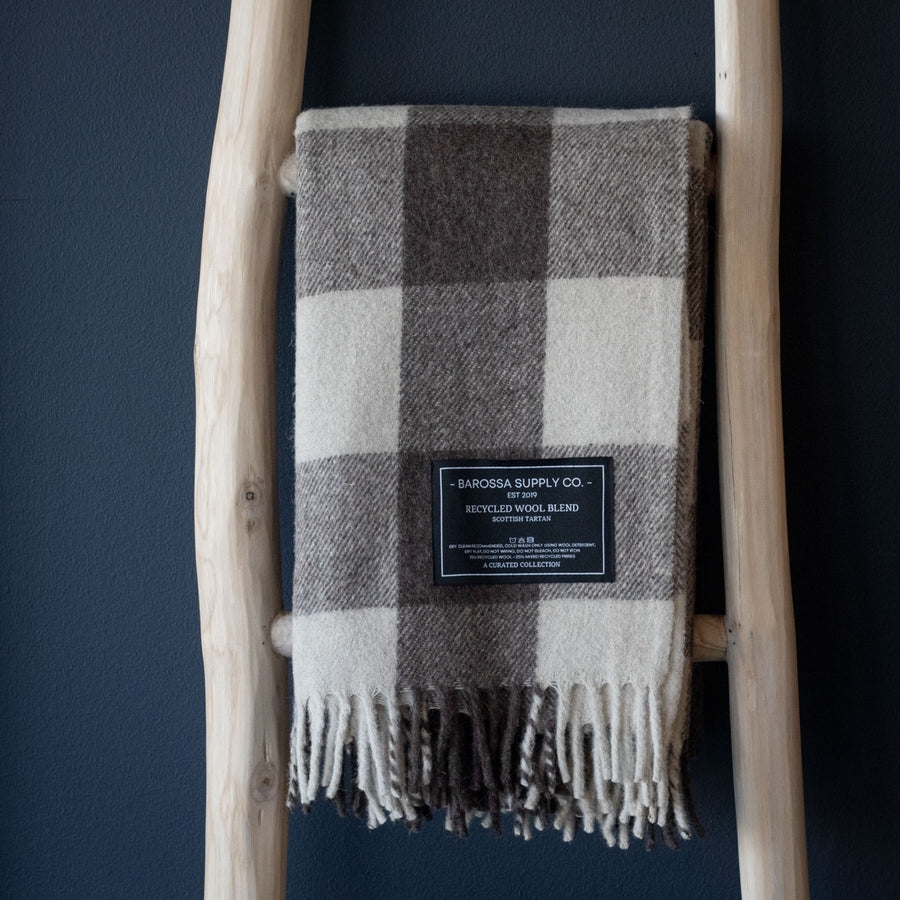 Plaid blanket with a label on a wooden ladder against a dark blue wall