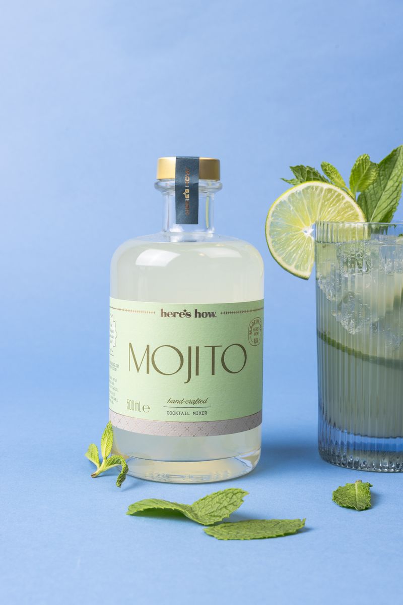 Bottle of Mojito with a glass of mojito and lime on a blue background