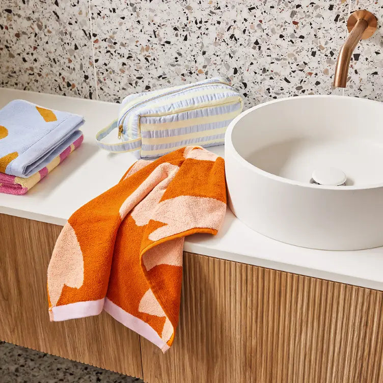 Bathroom setting with a white sink, orange towel, and folded towels on a wooden vanity.