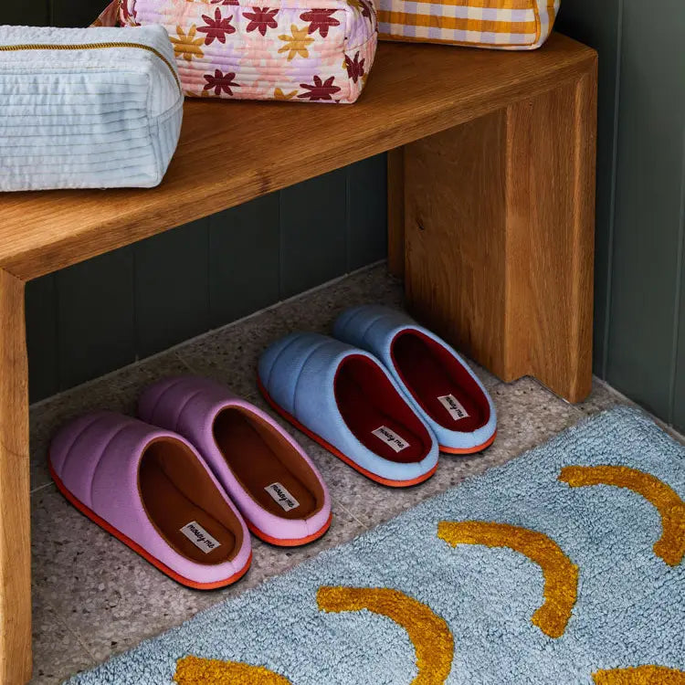 Pair of colorful slippers on a rug next to a wooden bench with bags.