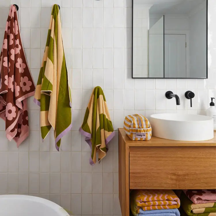 Bathroom with colorful towels hanging on a tiled wall, wooden vanity, and white sink.